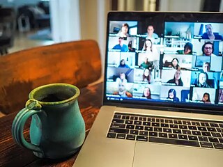 A laptop running an online event and a large green cup to the left of it.